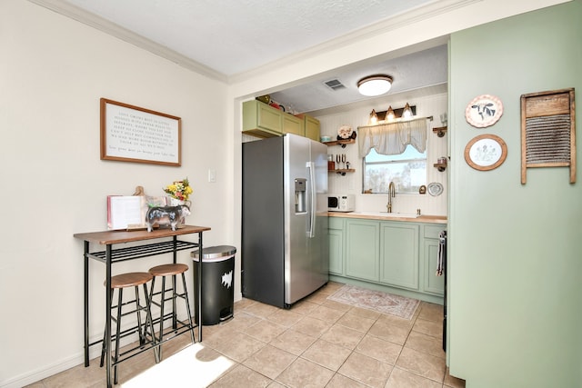 kitchen featuring green cabinets, stainless steel fridge, crown molding, and sink