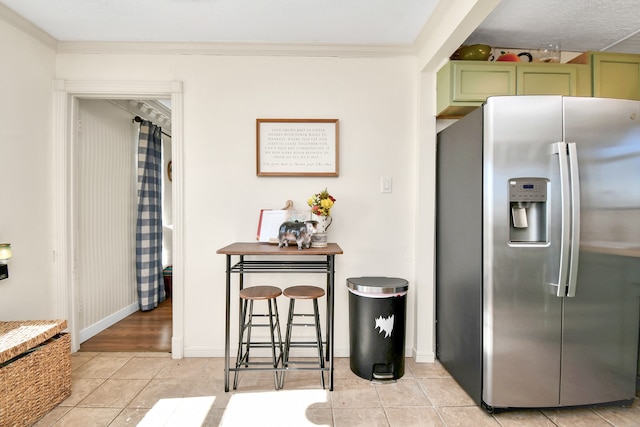 kitchen featuring green cabinets, stainless steel fridge with ice dispenser, crown molding, and light tile patterned floors