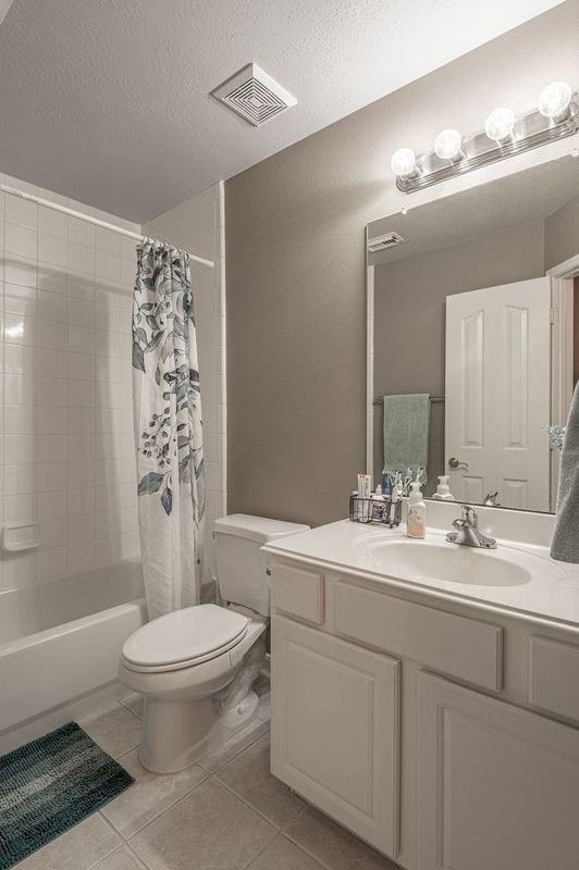 full bathroom featuring tile patterned floors, shower / bath combination with curtain, a textured ceiling, and toilet