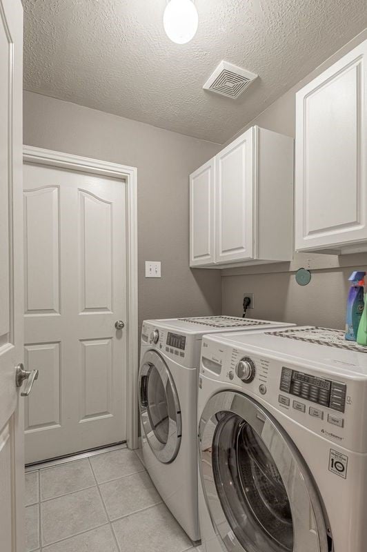 laundry area featuring cabinets, independent washer and dryer, a textured ceiling, and light tile patterned floors