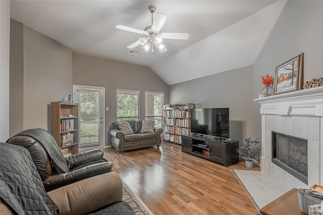 living room featuring light wood-type flooring, vaulted ceiling, ceiling fan, and a tiled fireplace