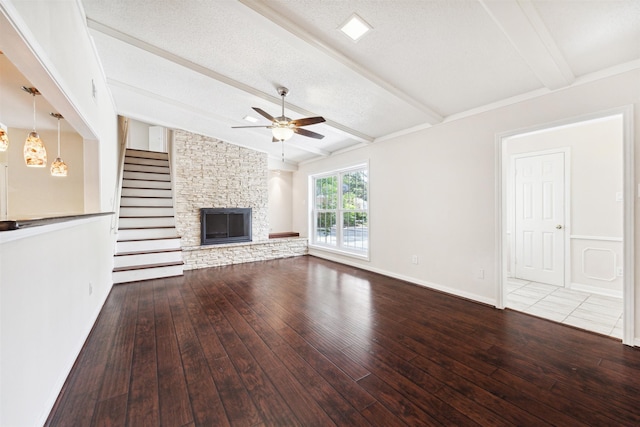 unfurnished living room with ceiling fan, a stone fireplace, lofted ceiling with beams, a textured ceiling, and hardwood / wood-style flooring