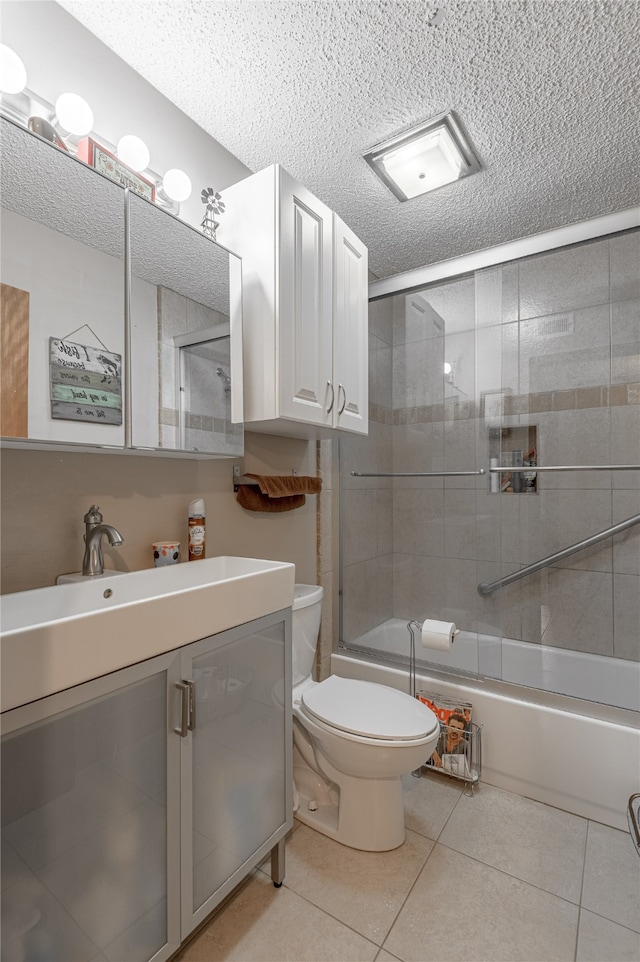 full bathroom featuring combined bath / shower with glass door, tile patterned flooring, vanity, a textured ceiling, and toilet