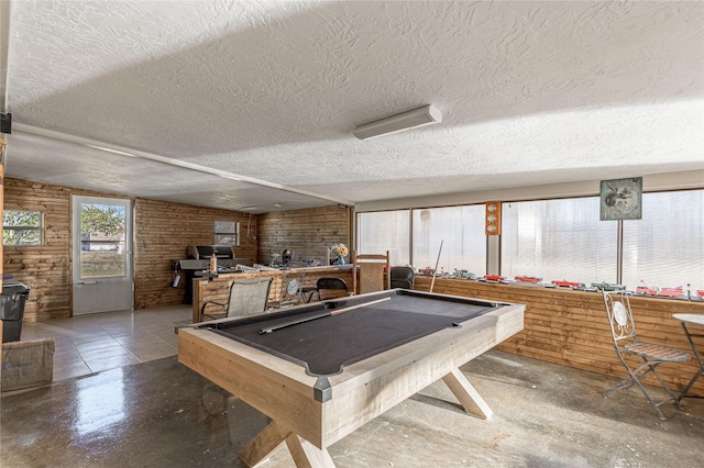 game room featuring billiards, wooden walls, a textured ceiling, brick wall, and a wood stove