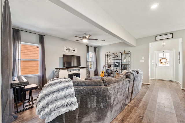 living room featuring ceiling fan, beam ceiling, wood-type flooring, and a fireplace