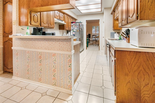 kitchen featuring kitchen peninsula, sink, light tile patterned flooring, and appliances with stainless steel finishes