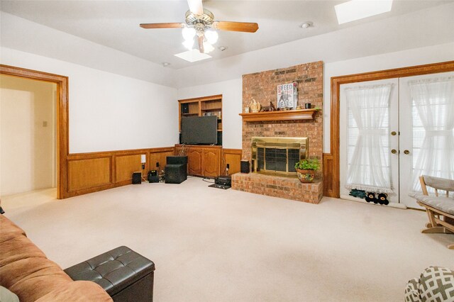 living room with carpet flooring, ceiling fan, wooden walls, and a brick fireplace