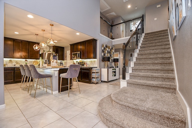 kitchen with a breakfast bar, dark brown cabinetry, stainless steel appliances, decorative light fixtures, and light tile patterned flooring