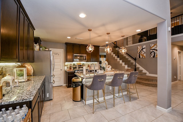 kitchen with pendant lighting, light stone countertops, appliances with stainless steel finishes, light tile patterned flooring, and a breakfast bar area