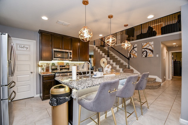 kitchen with light stone countertops, appliances with stainless steel finishes, decorative backsplash, dark brown cabinets, and decorative light fixtures