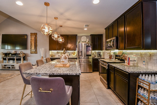 kitchen featuring a breakfast bar, backsplash, light stone countertops, an island with sink, and stainless steel appliances