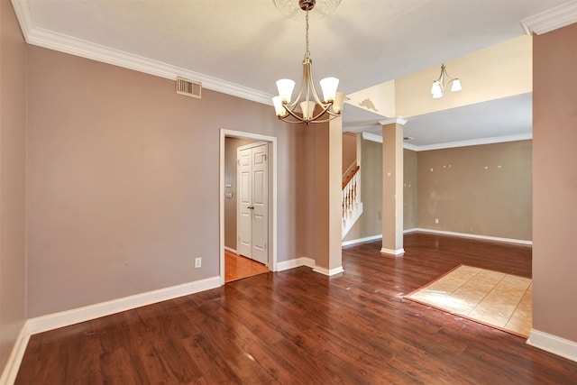 spare room featuring decorative columns, crown molding, a notable chandelier, and hardwood / wood-style flooring