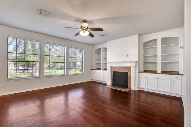 unfurnished living room featuring a tile fireplace, ceiling fan, dark hardwood / wood-style flooring, built in features, and a textured ceiling