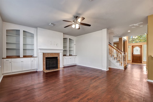 unfurnished living room with dark hardwood / wood-style floors, built in features, ceiling fan, and a tiled fireplace