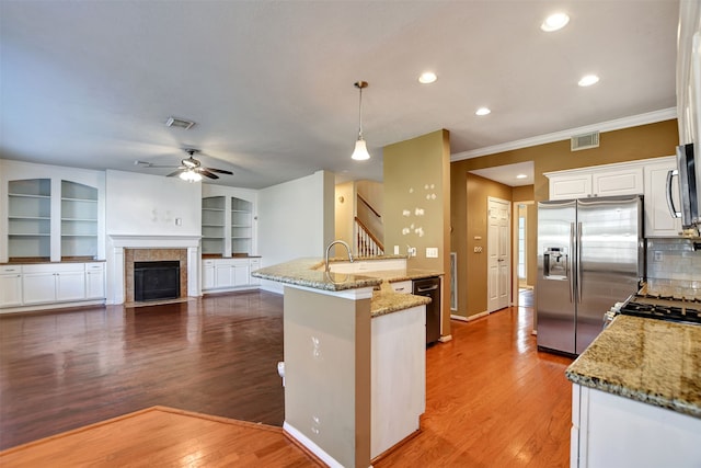 kitchen featuring hardwood / wood-style floors, appliances with stainless steel finishes, tasteful backsplash, decorative light fixtures, and light stone counters