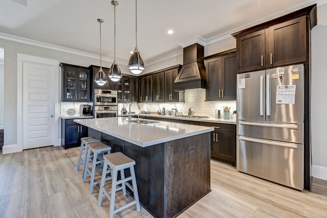 kitchen featuring custom range hood, dark brown cabinetry, stainless steel appliances, sink, and a center island with sink