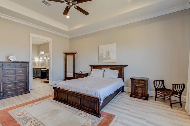 bedroom with ceiling fan, light hardwood / wood-style flooring, ensuite bathroom, a tray ceiling, and ornamental molding