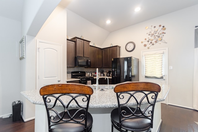 kitchen with dark brown cabinetry, vaulted ceiling, dark wood-type flooring, black appliances, and an island with sink