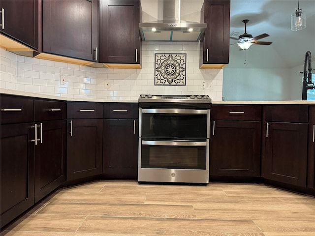 kitchen with light countertops, wall chimney range hood, light wood-style flooring, and double oven range