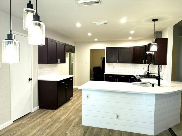 kitchen featuring pendant lighting, dark brown cabinets, kitchen peninsula, and backsplash