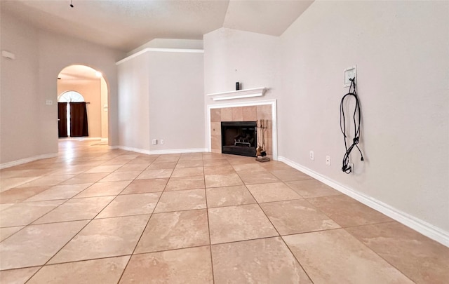 unfurnished living room featuring arched walkways, lofted ceiling, baseboards, and light tile patterned floors