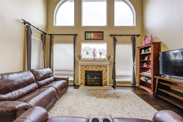 living room with a tile fireplace, a towering ceiling, and hardwood / wood-style flooring