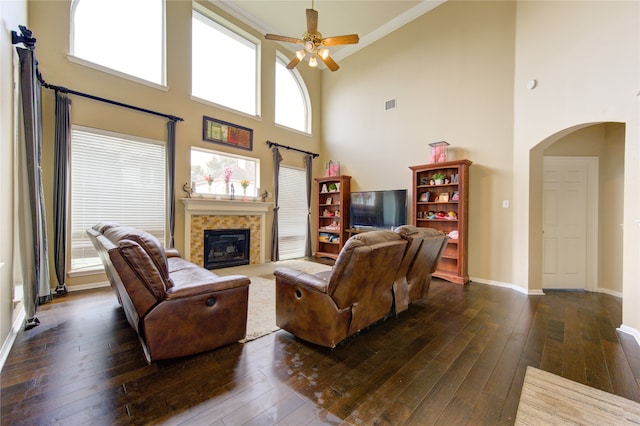 living room with a tiled fireplace, ceiling fan, dark hardwood / wood-style flooring, and a towering ceiling