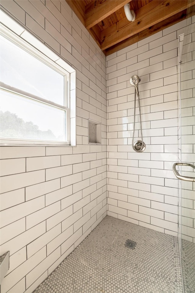 bathroom featuring beamed ceiling and a tile shower