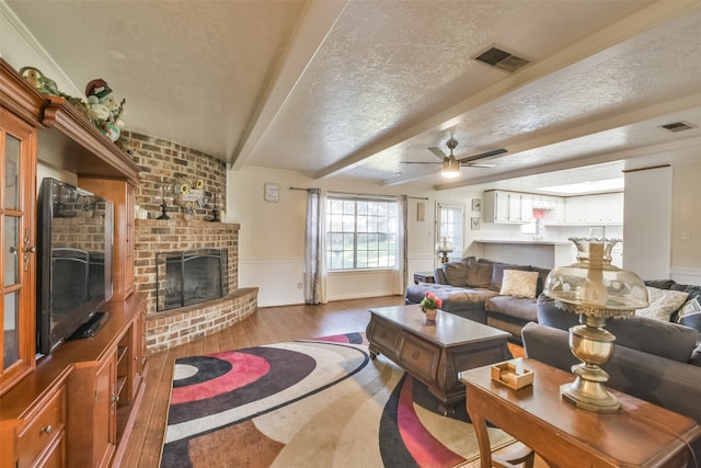 living room with ceiling fan, beamed ceiling, wood-type flooring, a textured ceiling, and a fireplace