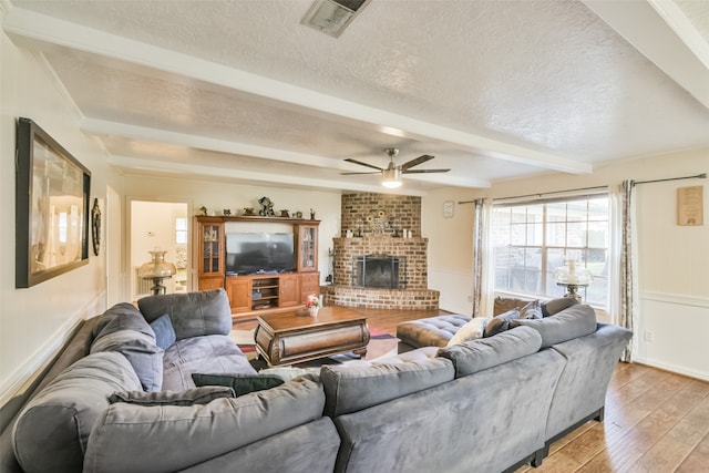 living room featuring a fireplace, a textured ceiling, ceiling fan, light hardwood / wood-style flooring, and beamed ceiling