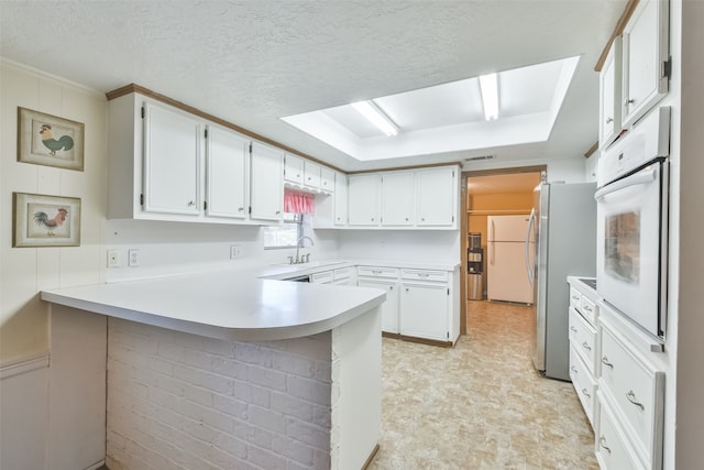 kitchen with kitchen peninsula, a textured ceiling, white appliances, sink, and white cabinetry