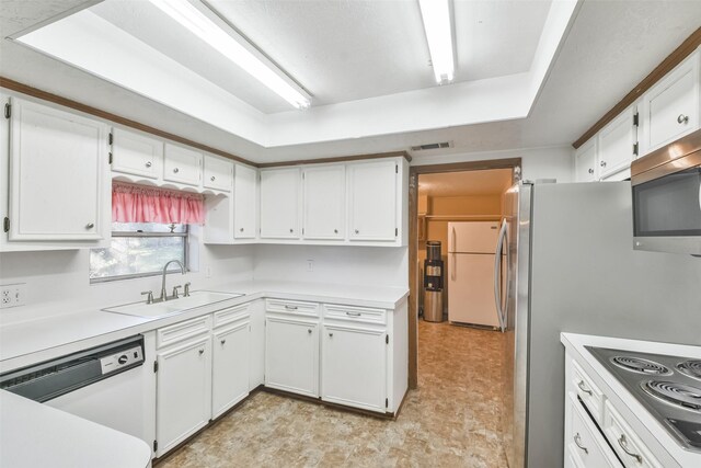 kitchen with white cabinets, white appliances, sink, and a tray ceiling