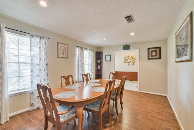 dining room featuring a healthy amount of sunlight, light hardwood / wood-style floors, and a textured ceiling