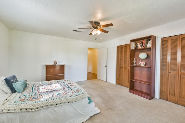 bedroom with two closets, ceiling fan, light carpet, and a textured ceiling