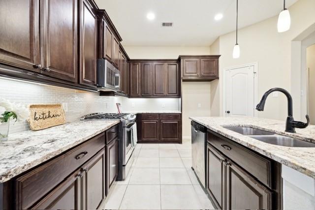 kitchen with sink, stainless steel appliances, tasteful backsplash, light stone counters, and pendant lighting