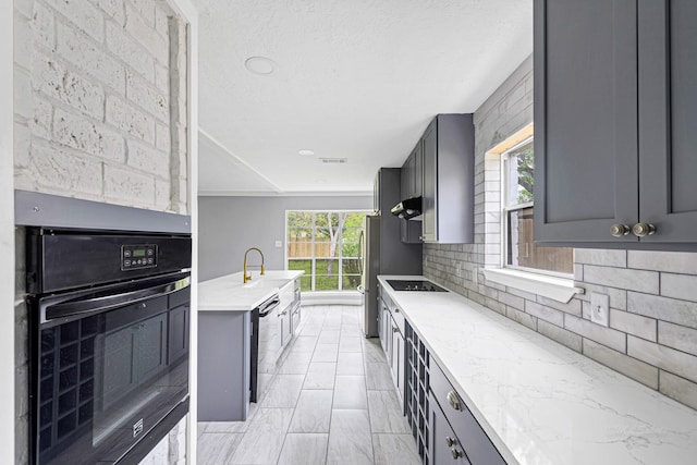 kitchen with sink, light stone counters, decorative backsplash, gray cabinets, and black appliances