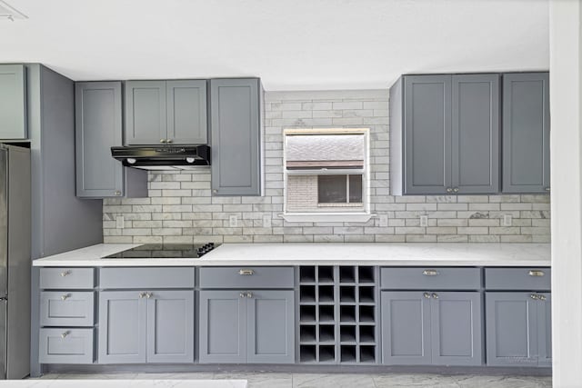 kitchen featuring gray cabinets, decorative backsplash, stainless steel refrigerator, light stone countertops, and black electric stovetop