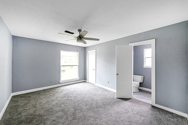 unfurnished bedroom with ensuite bath, ceiling fan, and dark carpet