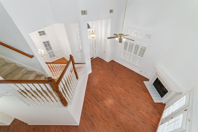 staircase featuring ceiling fan, wood-type flooring, a towering ceiling, and a fireplace