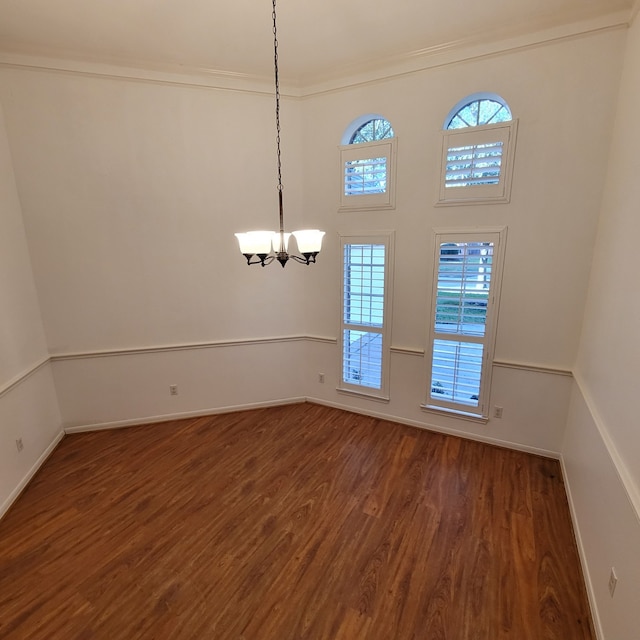 spare room featuring ornamental molding, an inviting chandelier, and dark wood-type flooring