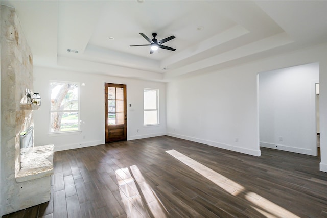 unfurnished living room featuring ceiling fan, a large fireplace, dark hardwood / wood-style flooring, and a tray ceiling