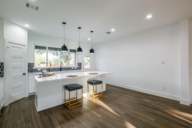 kitchen with dark wood-type flooring, white cabinets, hanging light fixtures, light stone countertops, and a kitchen island