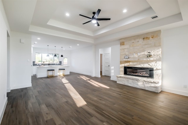 unfurnished living room with dark hardwood / wood-style floors, a raised ceiling, and a stone fireplace