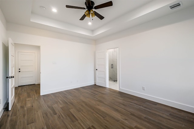 unfurnished room with a raised ceiling, ceiling fan, and dark wood-type flooring