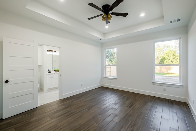 empty room with a raised ceiling, ceiling fan, dark hardwood / wood-style flooring, and plenty of natural light