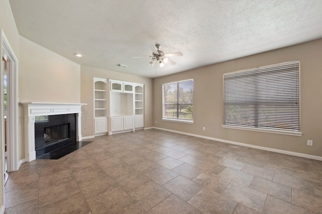 unfurnished living room featuring ceiling fan, built in features, a tile fireplace, and a textured ceiling