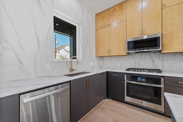 kitchen with tasteful backsplash, a sink, light wood-type flooring, appliances with stainless steel finishes, and light stone counters