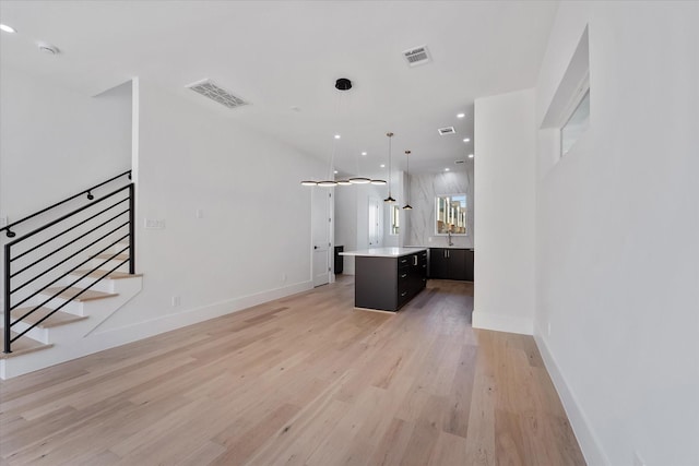 unfurnished living room featuring baseboards, visible vents, light wood-type flooring, and a sink