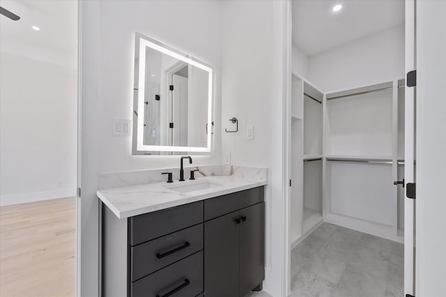bathroom with vanity, baseboards, a spacious closet, and recessed lighting