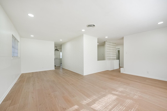 unfurnished room with light wood-type flooring and brick wall